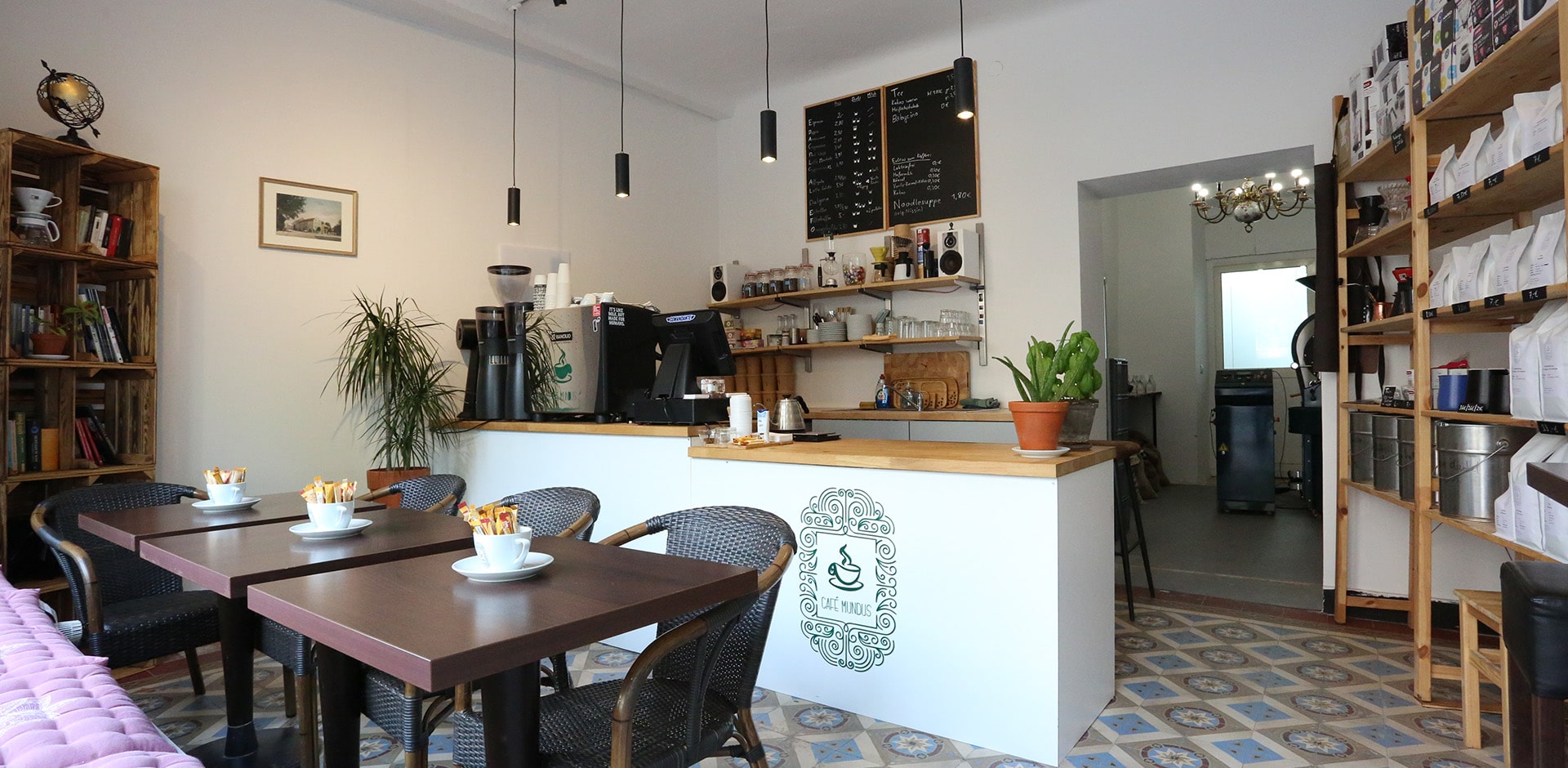 Eine Totalansicht des Café Mundus mit Tischen, Theke, Kaffeeregal, Espressomaschine und Bücherregal
