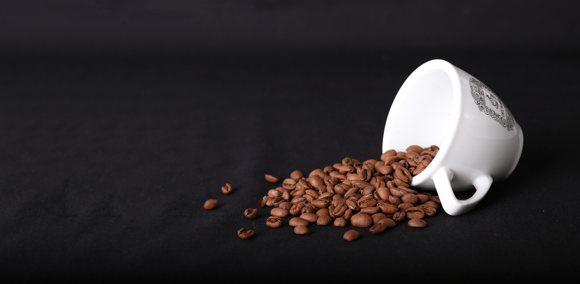 Eine weiße, liegende Espressotasse aus dem Café Mundus mit herausfallenden gerösteten Kaffeebohnen
