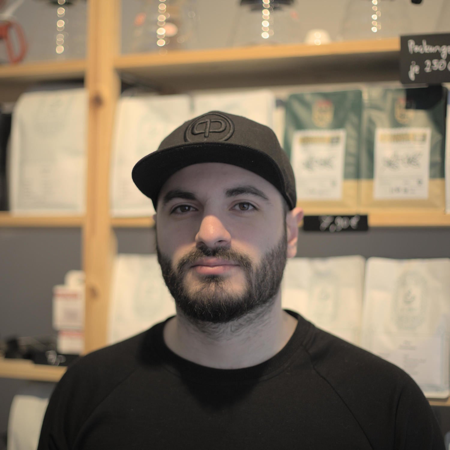 Ein Portrait von Enes Erdoğan vor einem Regal mit Kaffeetüten